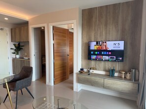 Un salon moderne avec un téléviseur à écran plat, une table basse en verre, un fauteuil en cuir marron et un meuble en bois.