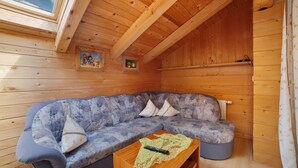 Interior de una cabaña de madera con sofá, una mesita y un tragaluz.