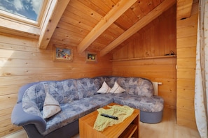 Interior de una cabaña de madera con sofá, una mesita y un tragaluz.