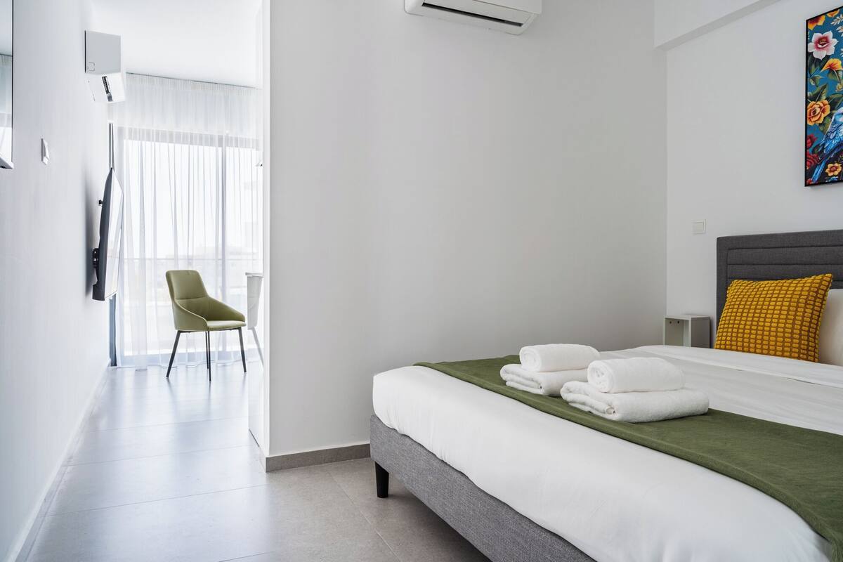 A hotel room with a bed, a chair, a TV, and a painting on the wall.