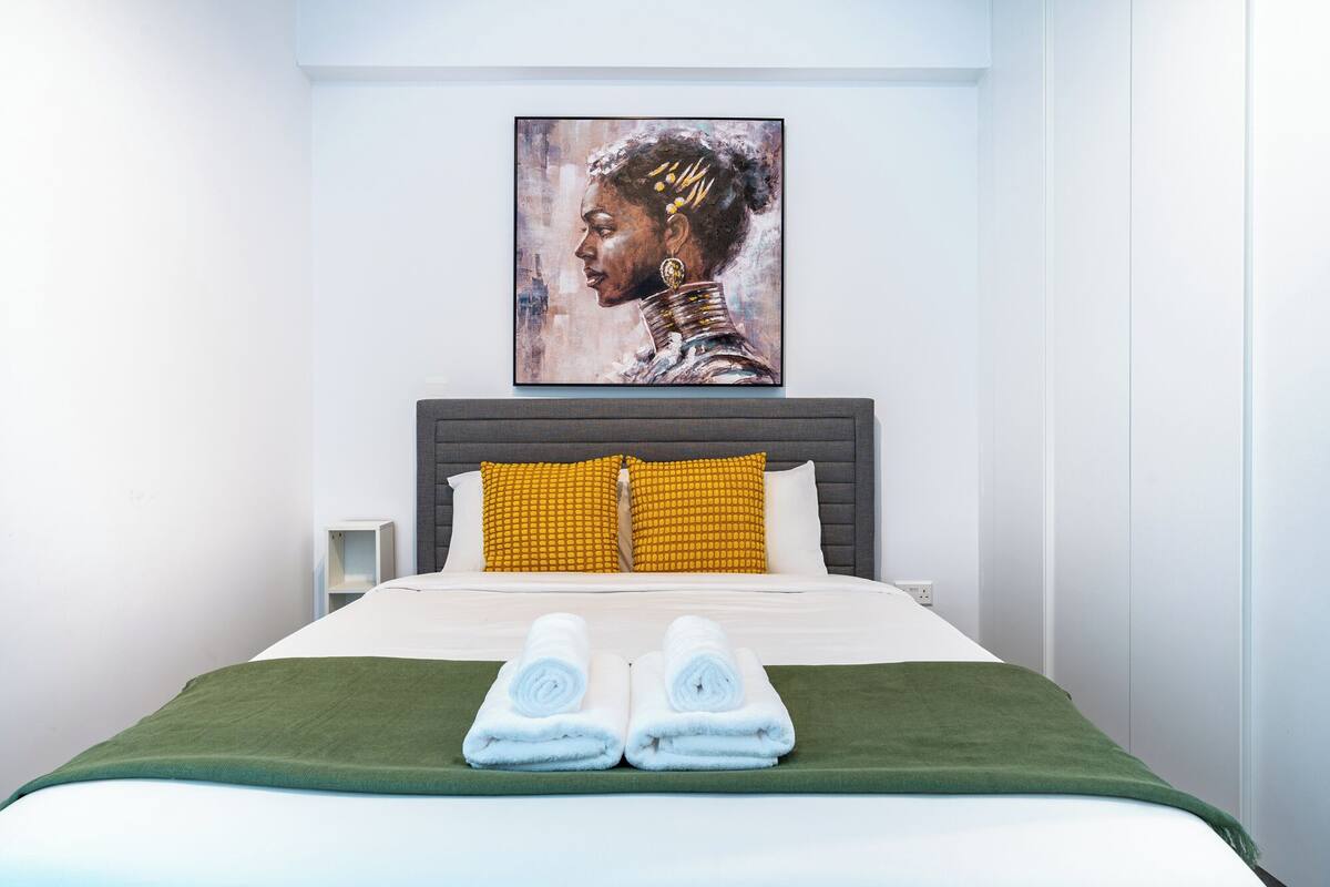 A hotel room with a bed, pillows, a painting on the wall, and towels on the bed.