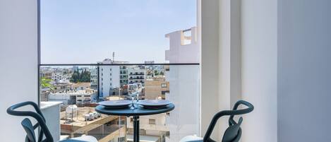 A balcony with a table and chairs, a clear view of the cityscape, and a modern building in the background.