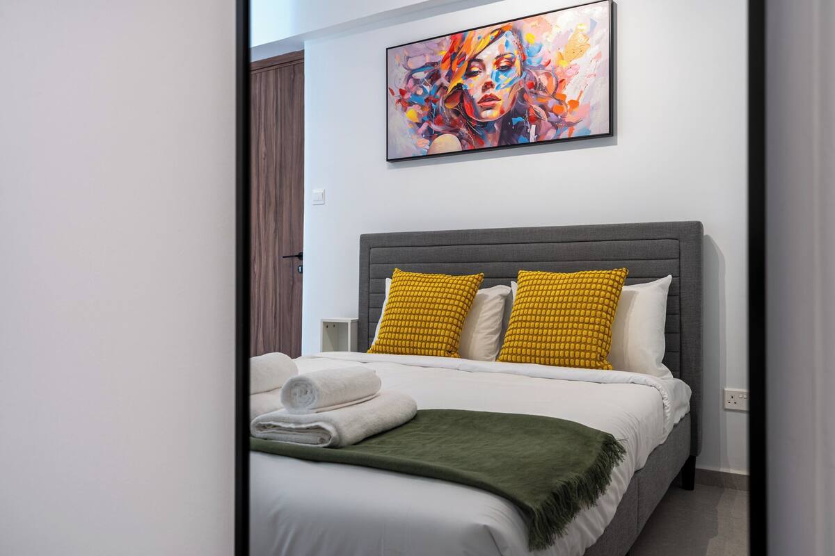A modern bedroom with a grey headboard, white bedding, and a colorful abstract painting above the bed.