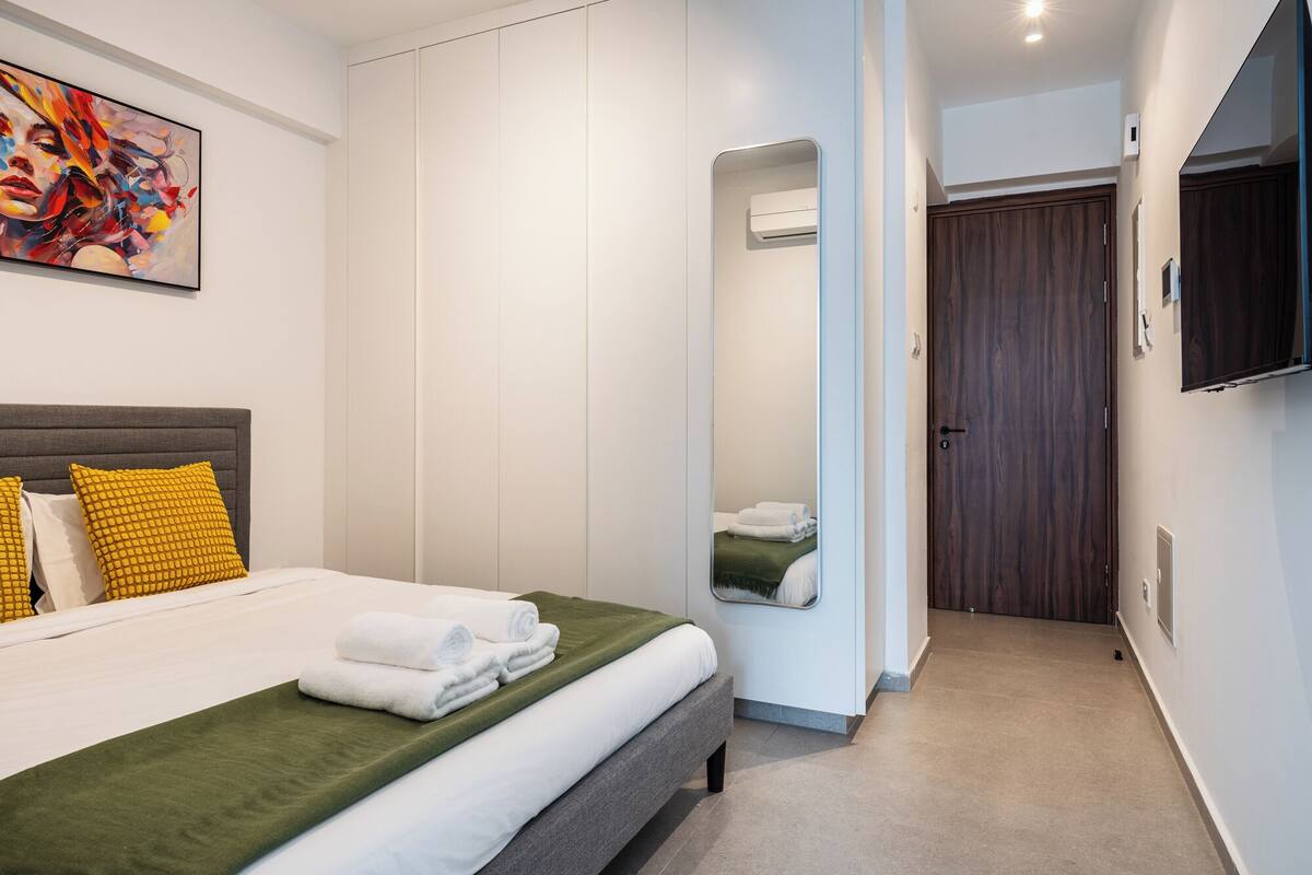 A modern hotel room with a large bed, a mirror, a wardrobe, and a television.