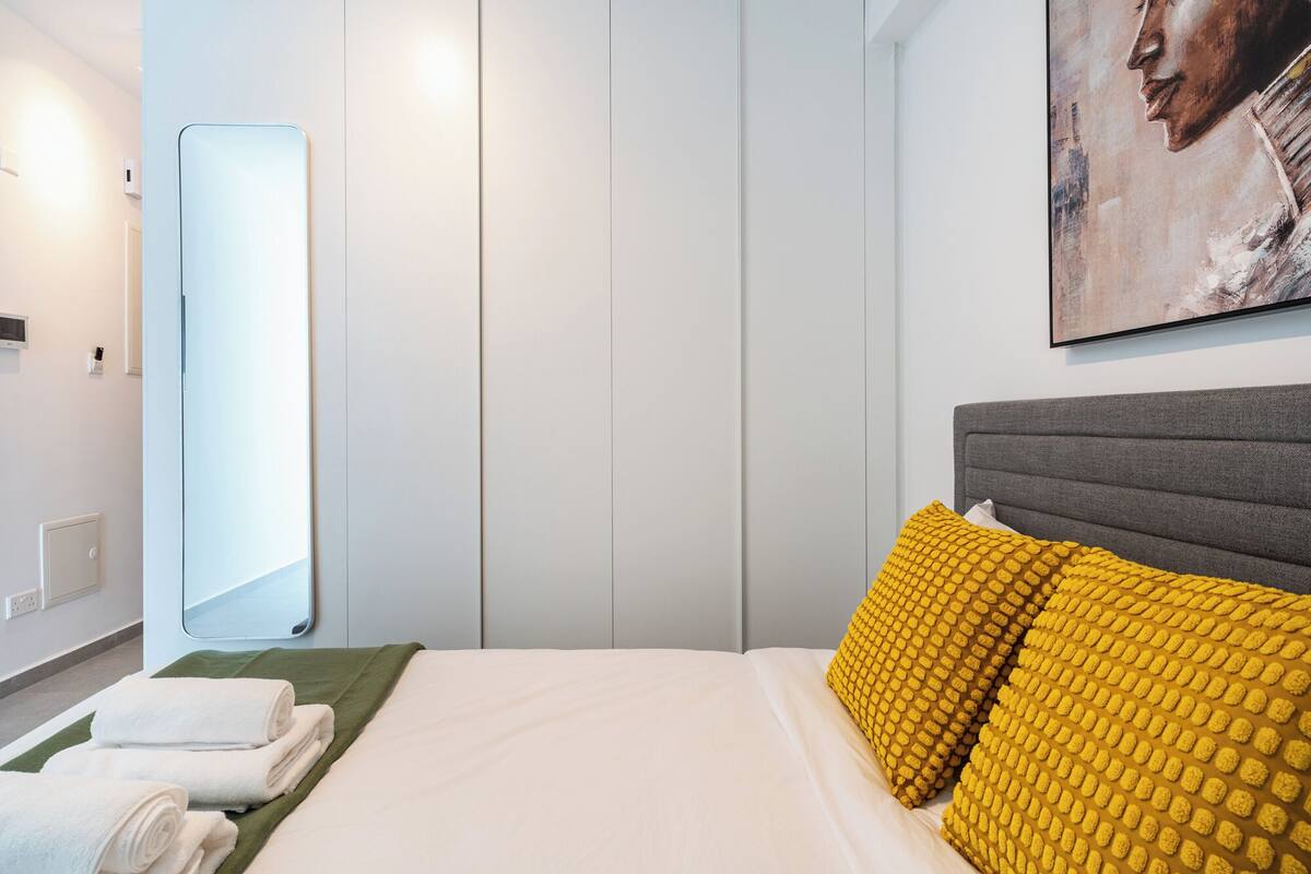 A hotel room with a bed, a large mirror, a painting on the wall, and a green area rug.