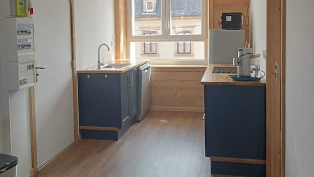 Eine kompakte Küche mit Holzausstattung, einem eingebauten Backofen und einem Fenster mit Blick auf eine Wohngegend.