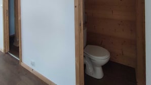 Ein Zimmer mit Holzboden, weißen Wänden und einer Toilette, die durch eine Holzwand abgetrennt ist.
