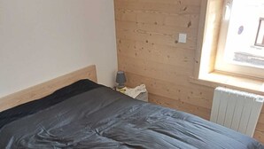 Ein Zimmer mit einem Bett, Holzwänden, einem Heizkörper und einem Fenster.