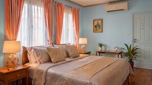 A bedroom with a bed, two bedside tables with lamps, a nightstand, a potted plant, and a door.