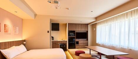 A hotel room with a bed, a desk, a kitchenette, and a large window with curtains.