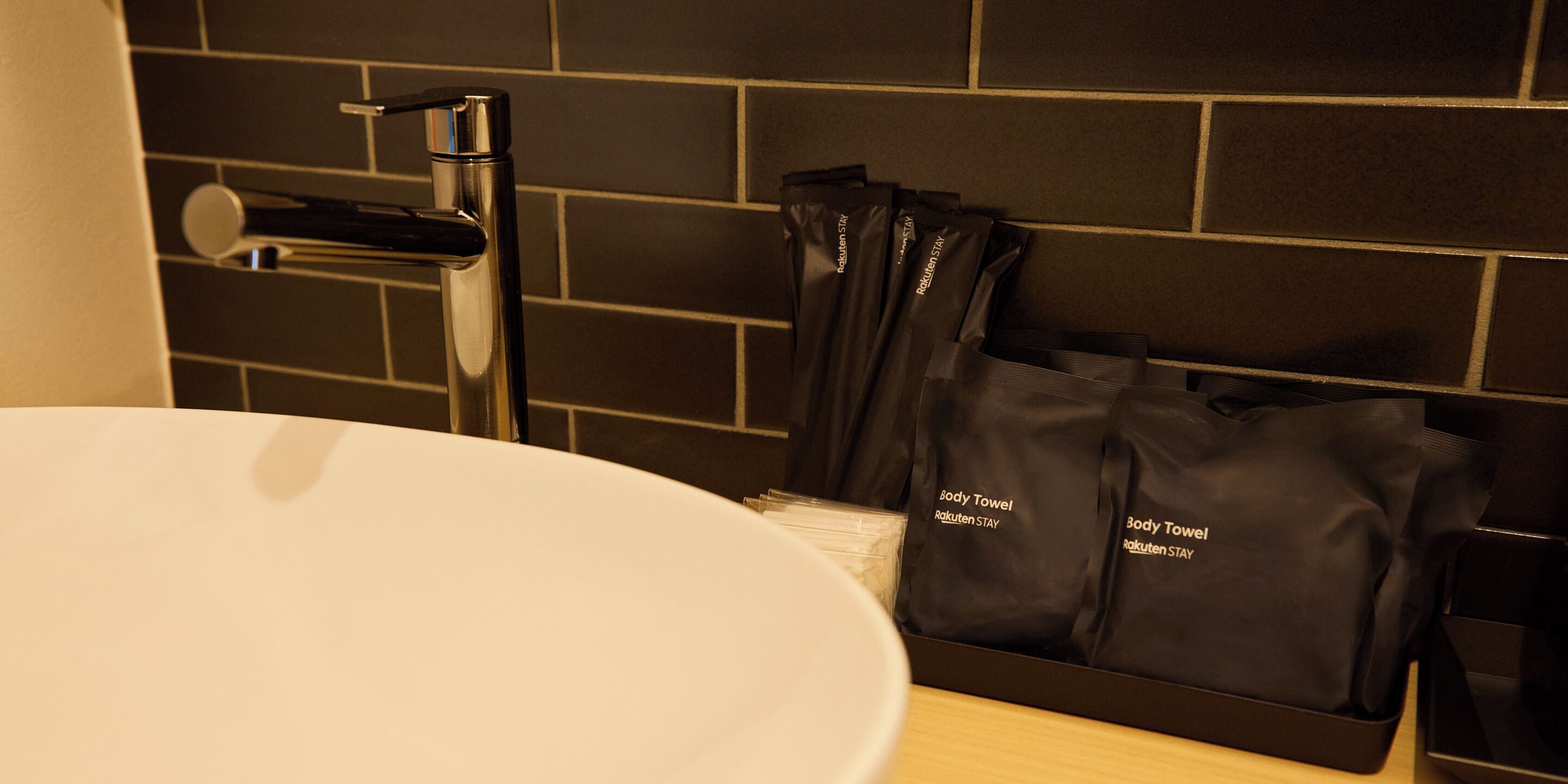 A bathroom with a white sink, a modern faucet, and a black towel rack holding several black towels.