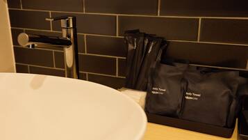 A bathroom with a white sink, a modern faucet, and a black towel rack holding several black towels.