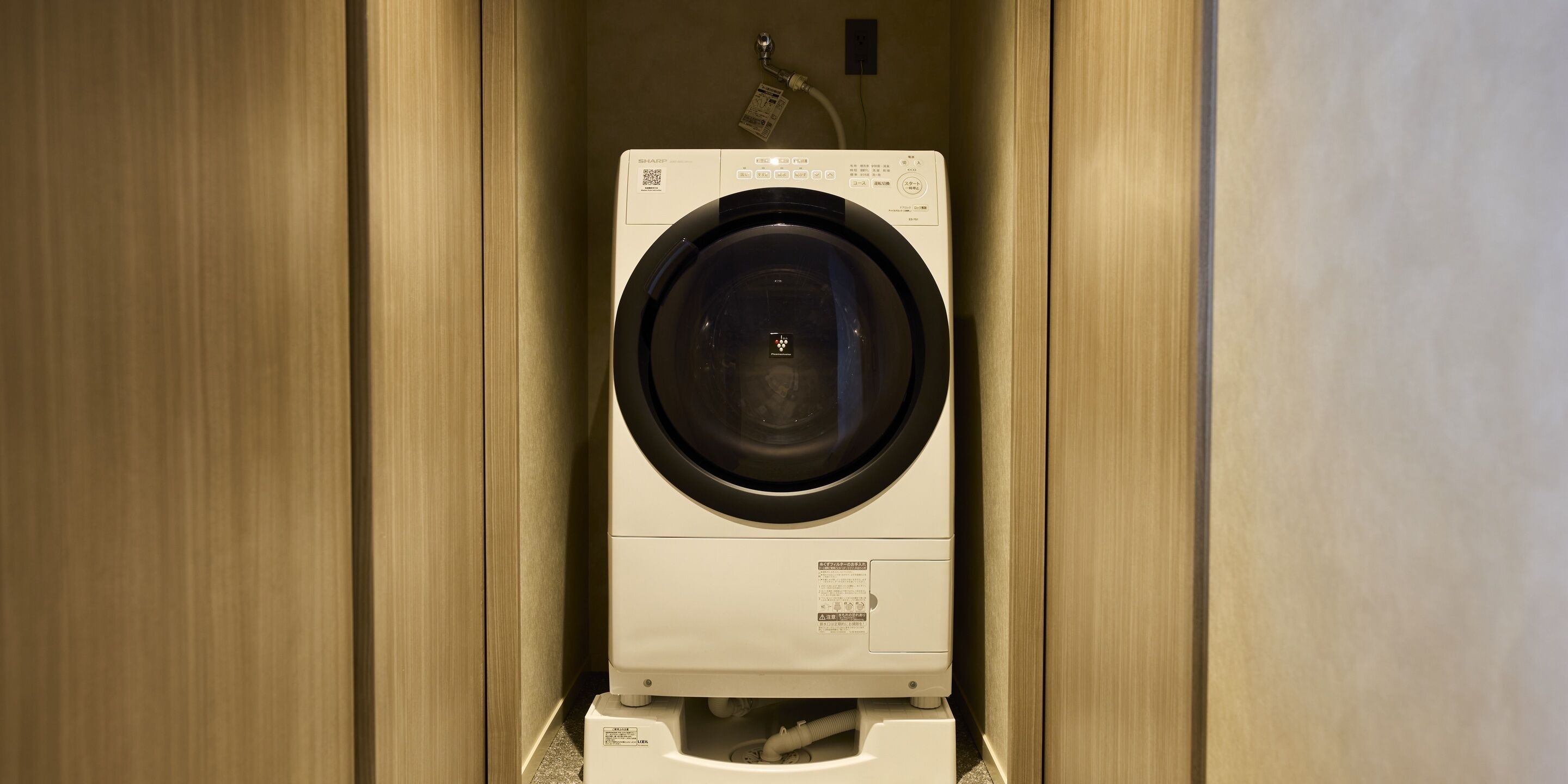 Een compacte, aan de muur bevestigde wasmachine in een smalle ruimte met houten lambrisering.