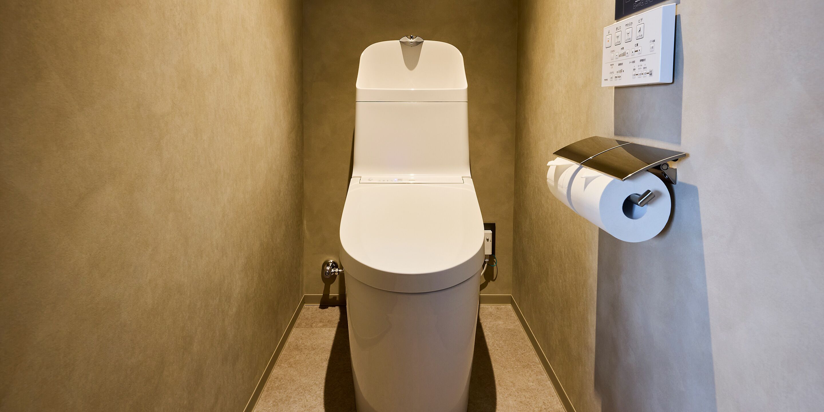 Eine Toilette mit Spülhebel, Toilettenpapierhalter und einer an der Wand montierten Steckdose.