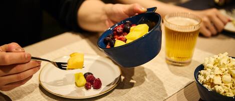 A dining table with a bowl of fruit, a glass of beer, and a bowl of popcorn.