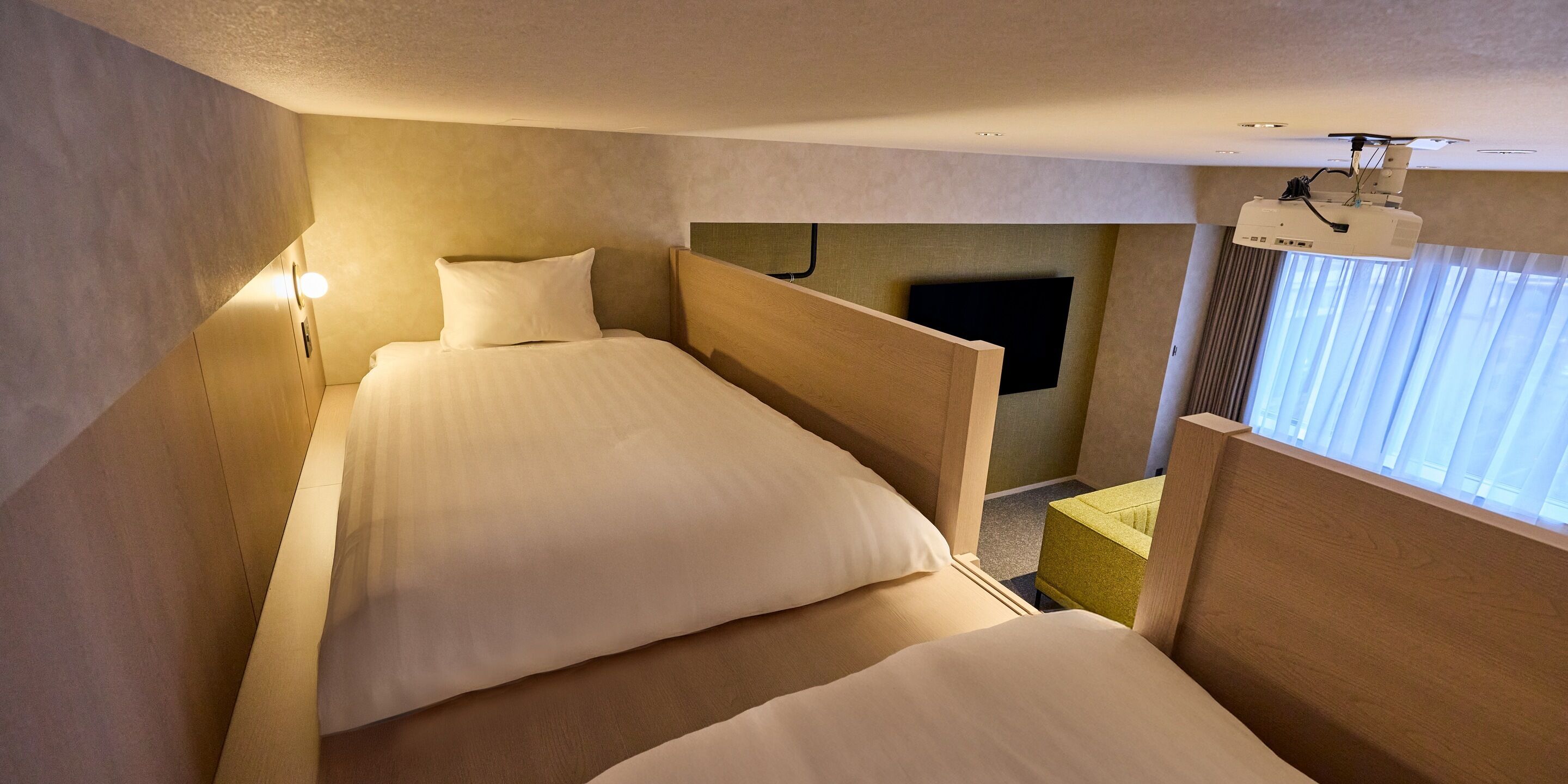 Ein Hotelzimmer mit zwei Betten, einem Fernseher und einem an der Decke befestigten Projektor.