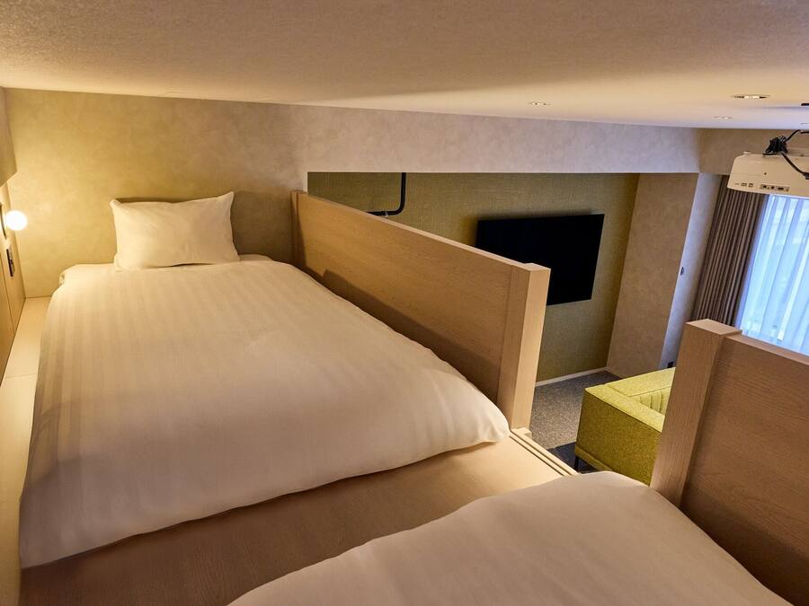 Ein Hotelzimmer mit zwei Betten, einem Fernseher und einem an der Decke befestigten Projektor.