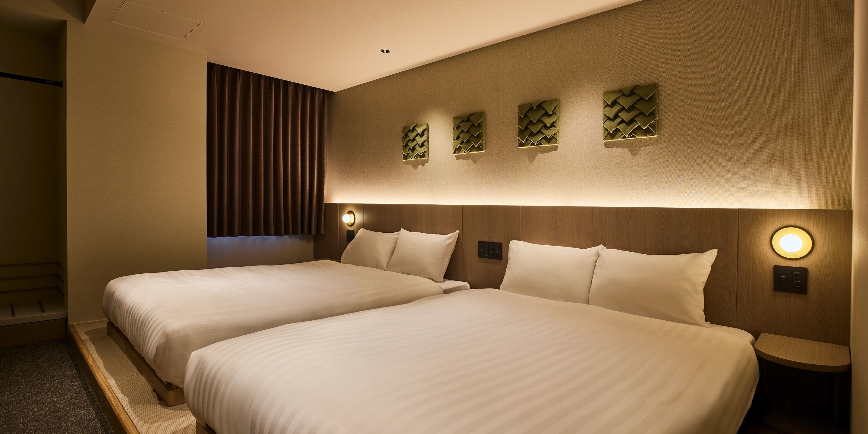 A hotel room with two beds, a wall-mounted light, and a wooden headboard.