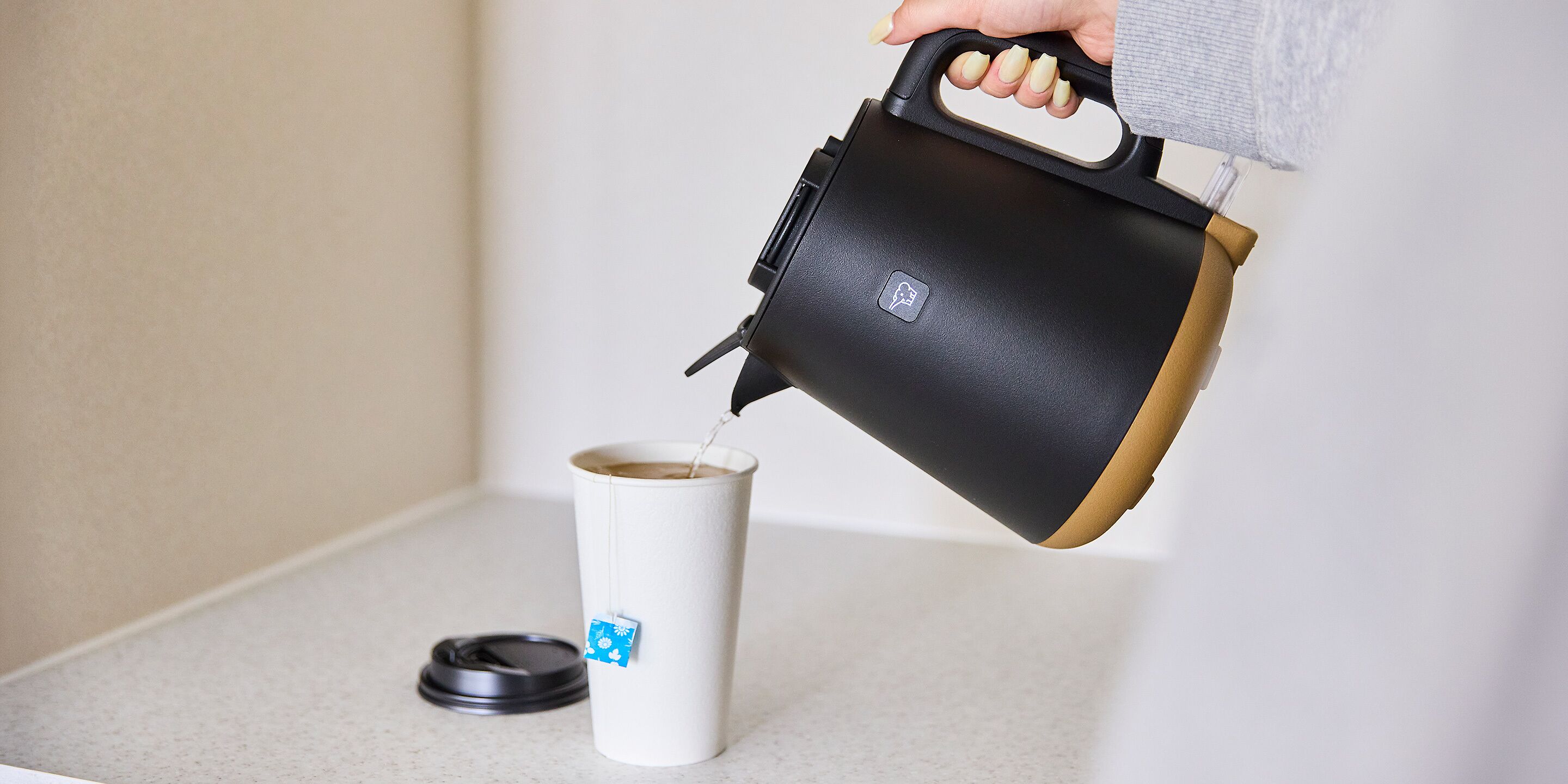 Une main verse un liquide d’un thermos noir et marron dans un gobelet blanc doté d’un couvercle.