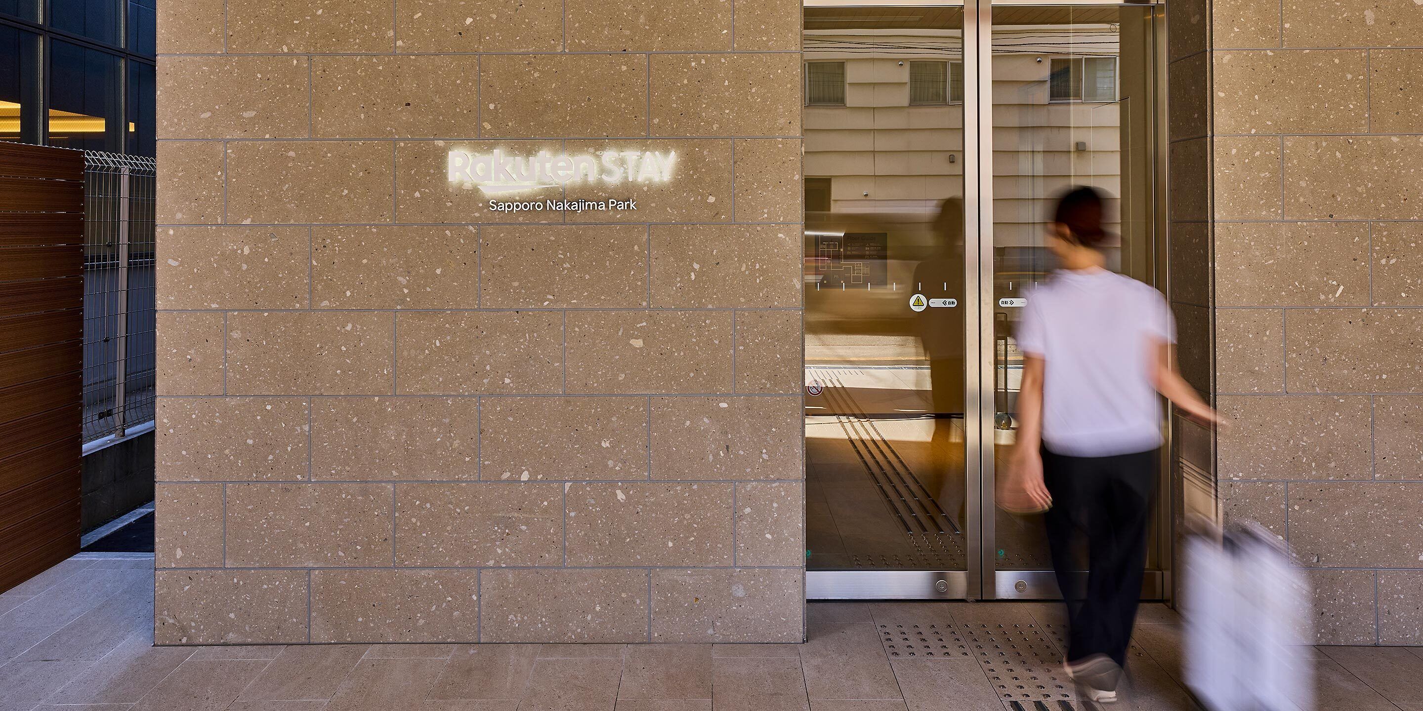 A building entrance with a sign reading 'Pakuten Stay' and 'Sapporo Nakajima Park'.