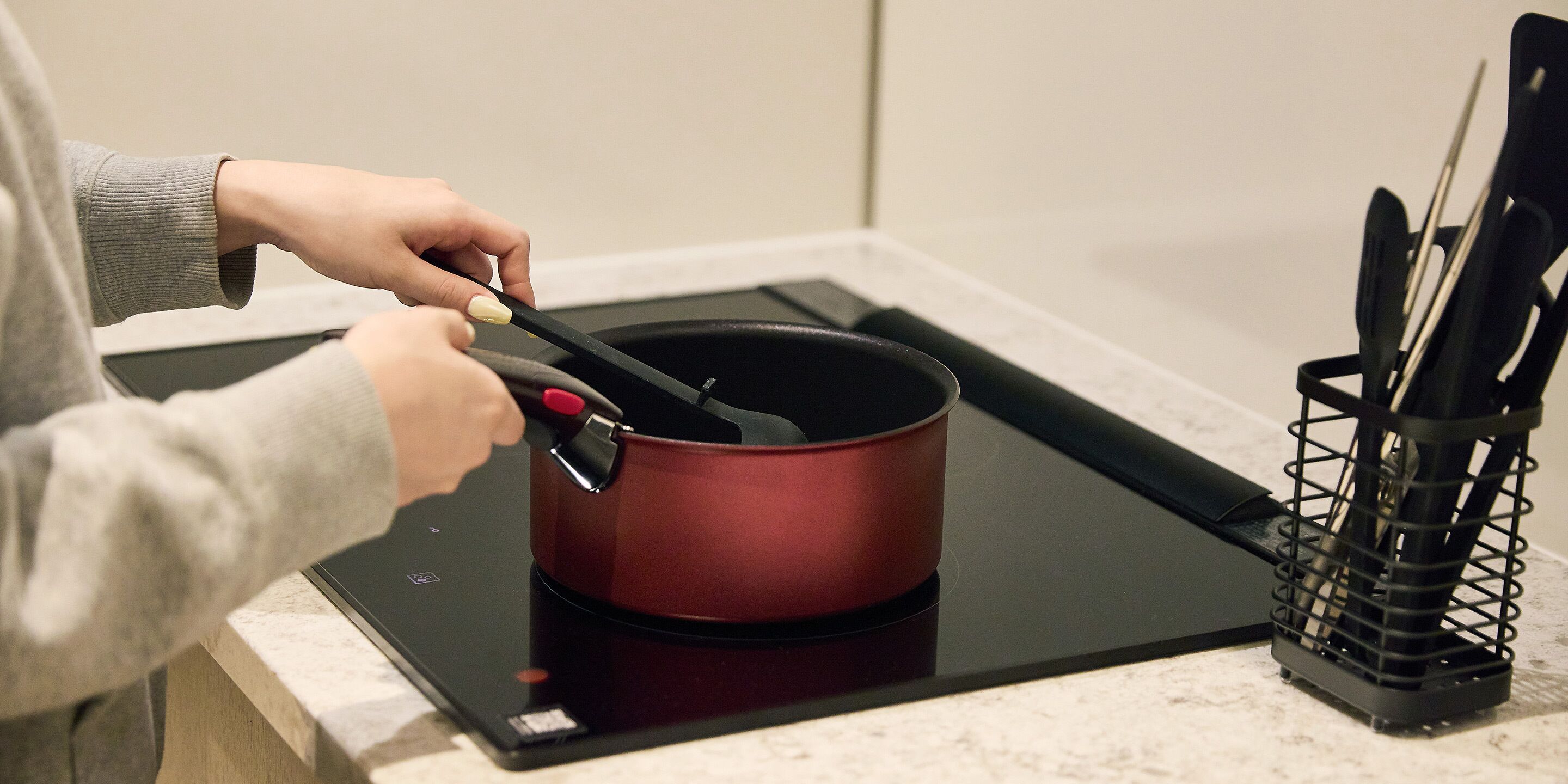 A person cooking on an induction cooktop with a pot and a utensil holder nearby.
