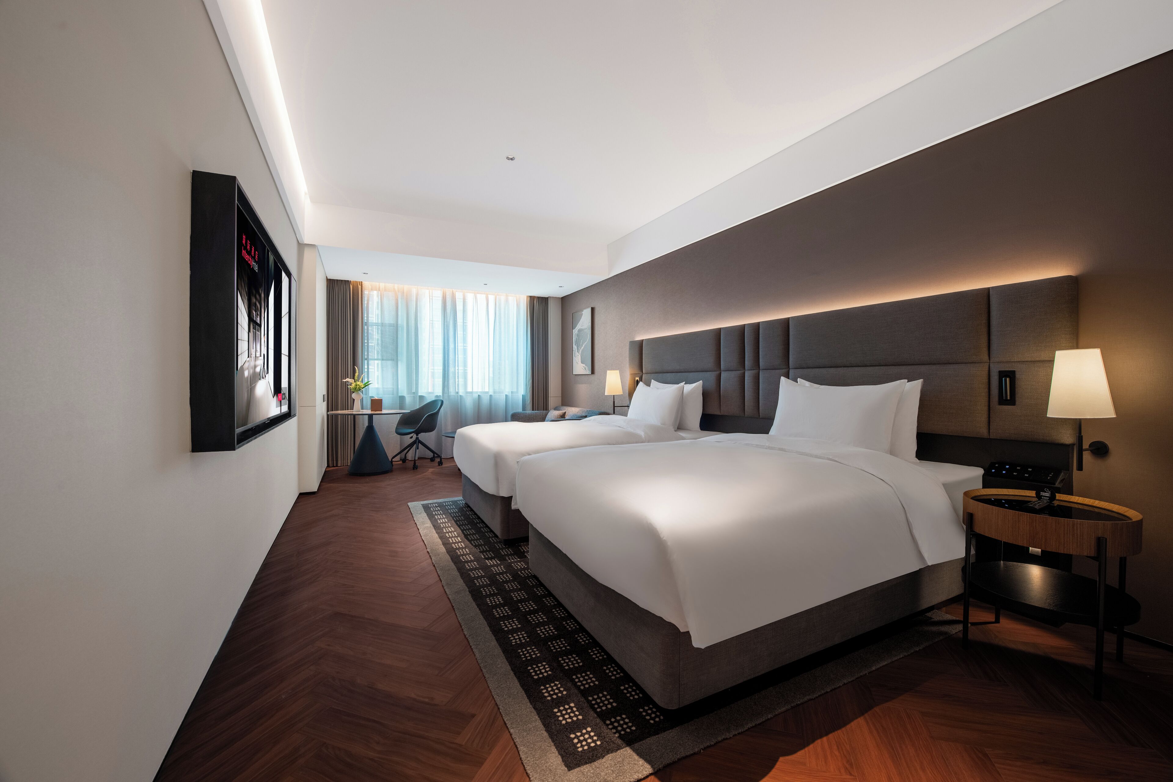 Una habitación de hotel con una cama grande, mesitas de noche, un escritorio y vista a la ciudad.