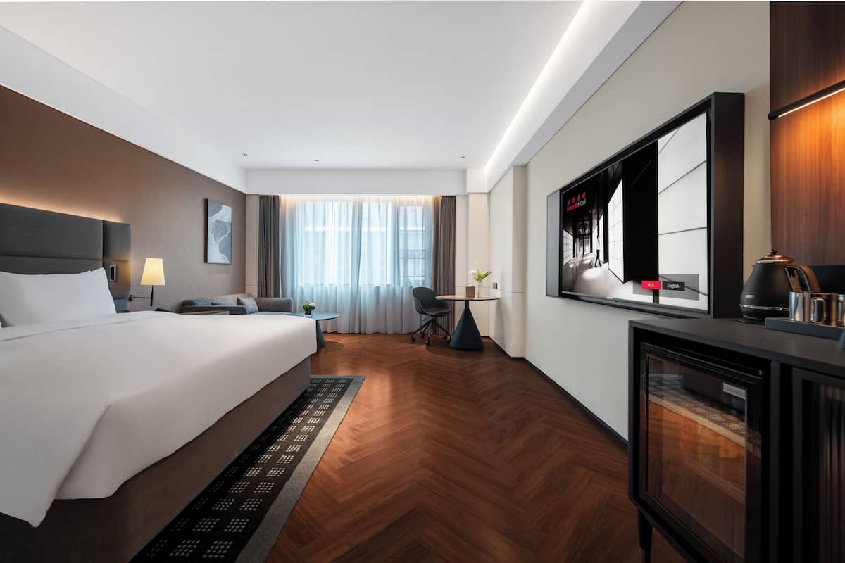 Habitación de hotel con cama, escritorio, silla, televisor y cafetera.