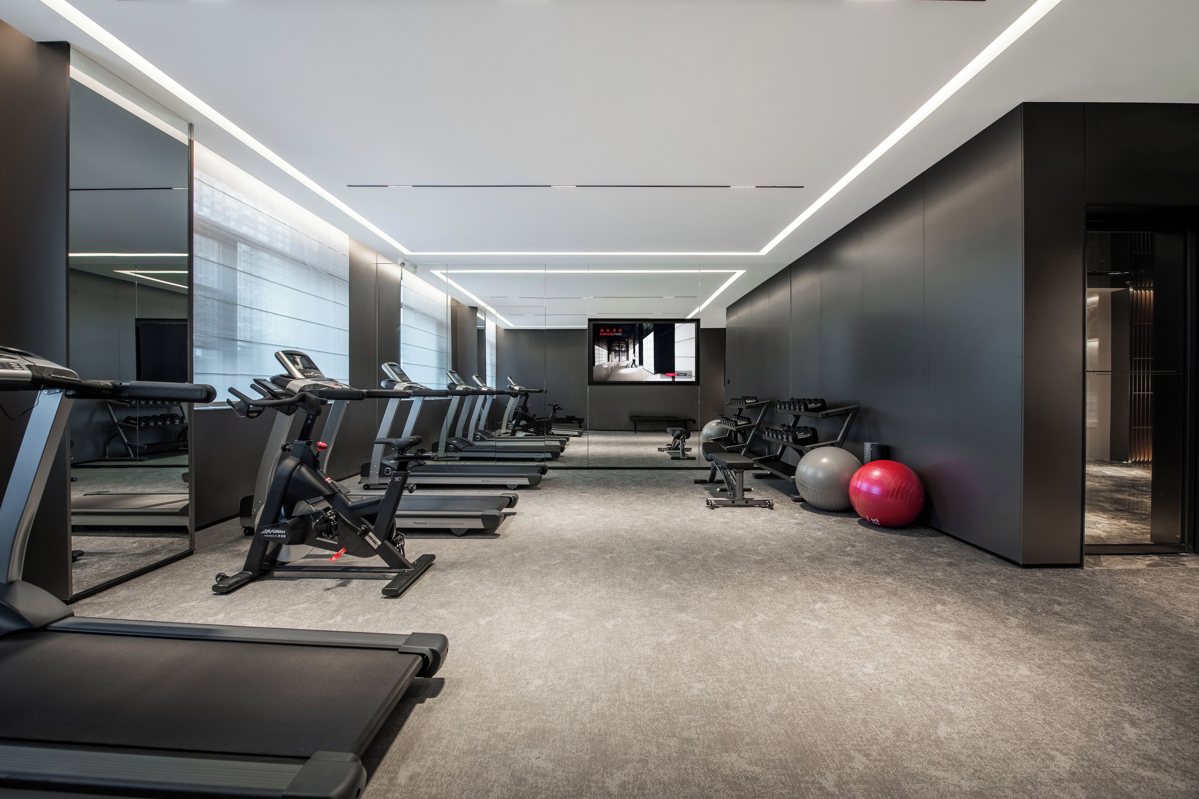 A modern gym with treadmills, exercise balls, and a TV screen.
