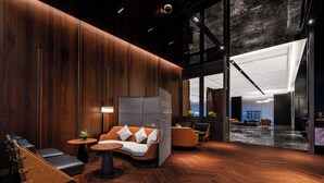 A modern interior with wooden paneling, a seating area with a sofa and chairs, a small table with a plant, and a large window.