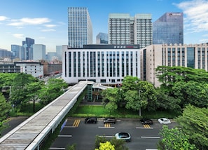 A modern building with a prominent entrance, surrounded by lush greenery and a pedestrian bridge.