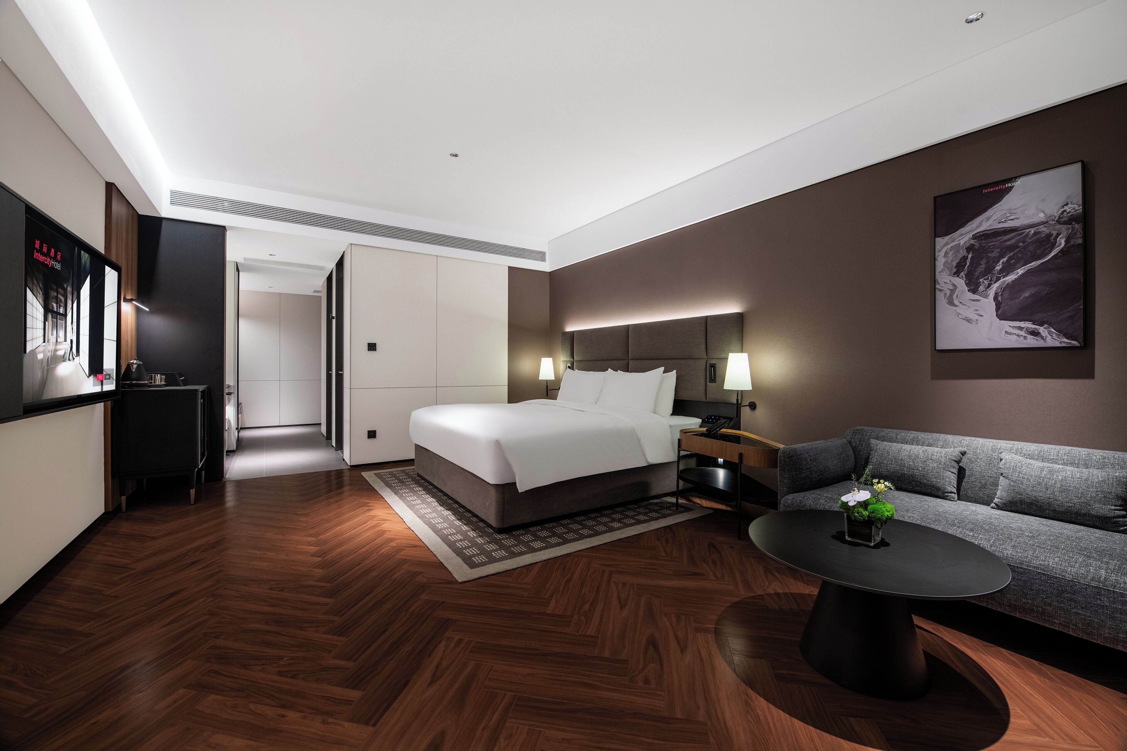 A modern hotel room with a bed, a sofa, a coffee table, a desk, and a TV.