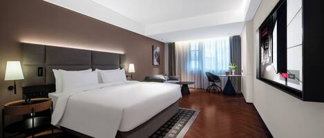 Quarto de hotel moderno com uma cama grande, mesas de cabeceira, escrivaninha e vista para a cidade.