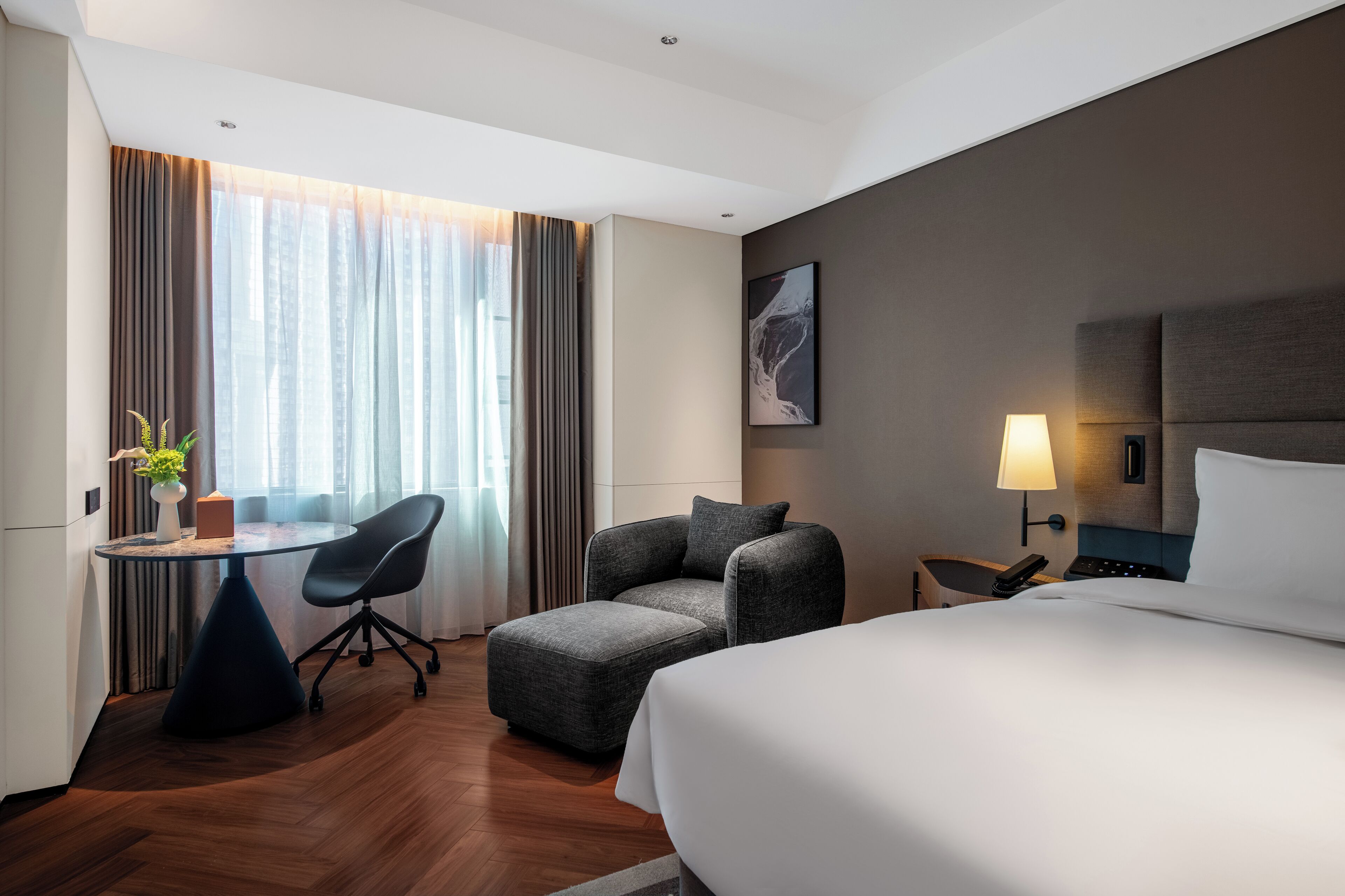 Ein Hotelzimmer mit Bett, Schreibtisch mit Stuhl, Lampe und einem Fenster mit Vorhängen.
