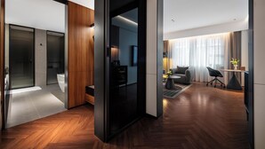 A modern hotel room with a wooden floor, a sofa, a coffee table, and a TV.