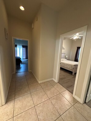 Ein Flur mit gefliestem Boden, der zu einem Schlafzimmer mit Bett und Deckenventilator führt.