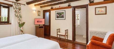 Quarto de hotel com cama, uma cadeira, televisão e área de chuveiro.