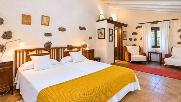 A bedroom with a double bed, two bedside tables, a nightstand, a chair, a small table, and a window with curtains. - Guestready - Hotel Rural Las Calas (Vega de San Mateo)