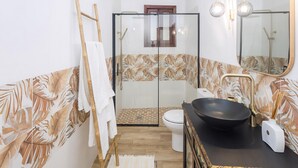 Un baño con cabina de ducha de vidrio, inodoro, lavabo con lavamanos negro y espejo con luces empotradas.