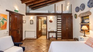 A hotel room with a loft bed, a sitting area with a chair, a small table with a lamp, and a bathroom visible through an open door. - Guestready - Hotel Rural Las Calas (Vega de San Mateo)