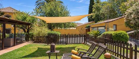 Une terrasse ensoleillée, aménagée à l’extérieur, avec une clôture en bois, un espace ombragé et un coin salon.