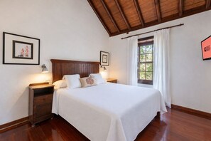 Ein Hotelzimmer mit einem hölzernen Bett, zwei Nachttischen, einem Fenster mit Vorhängen und gerahmten Bildern an den Wänden.