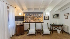 Una habitación con pared de piedra, televisión de pantalla plana, dos sillones, una mesita y un radiador.