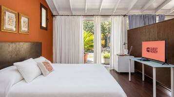 Habitación de hotel con cama, escritorio, televisor mostrando 'GUEST READY' y vistas al exterior.