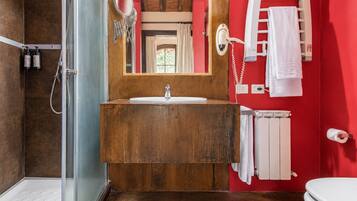 Een badkamer met een houten wastafelmeubel, een glazen douchecabine en een rode wand.