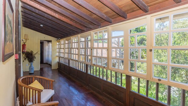 Un pasillo cubierto con vigas de madera y barandilla, que conduce a una habitación con ventanas amplias.