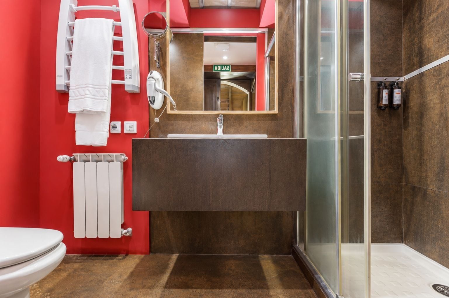 Un baño moderno con cabina de ducha de vidrio, inodoro blanco, toallero y espejo sobre el lavamanos.