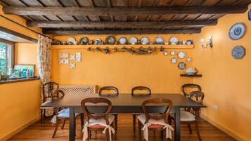 Un comedor con una mesa y sillas de madera, una pared amarilla y una variedad de platos y tazas exhibidos en estantes.