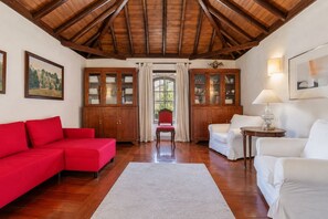 A room with a red sofa, white armchairs, a wooden cabinet, and a red chair. - Guestready - Hotel Rural Las Calas (Vega de San Mateo)