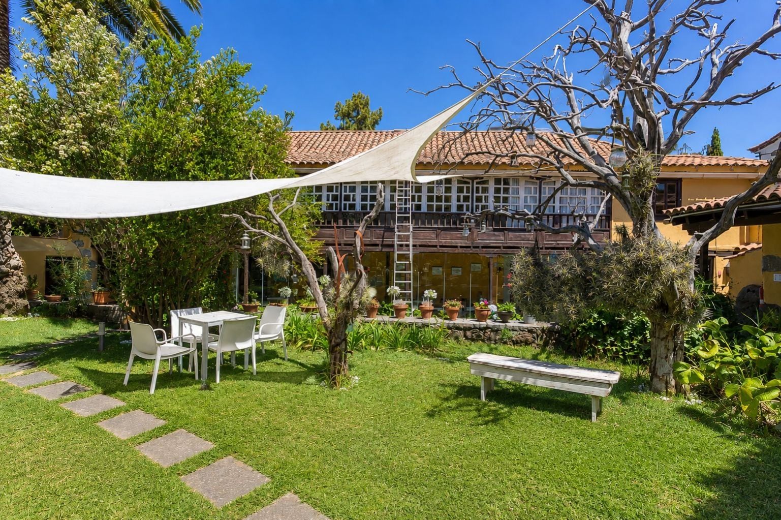 A courtyard with a white table and chairs, a bench, and a variety of potted plants.