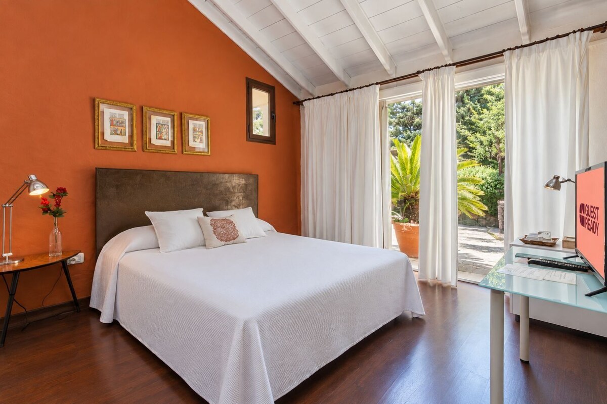 A hotel room with a bed, a desk with a computer, and a window with curtains.